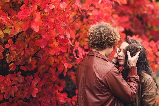 곱슬 머리 콧수염 남자와 붉은 나무에 대하여 가을에 포옹 갈색 머리 여자