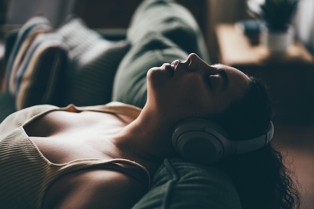 Foto giovane donna in sovrappeso con i capelli ricci sdraiata sul divano verde che ascolta musica con le cuffie wireless