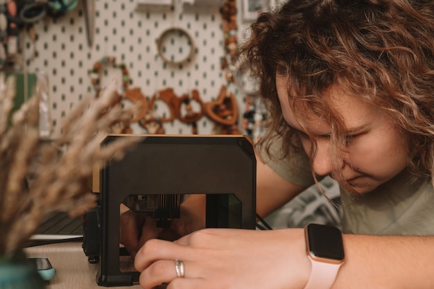 Photo curly haired woman holds item in desktop laser wood burning machine to inscribe name on surface of childrens wooden toy