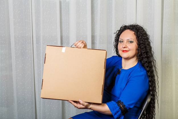 Curly joyful brunette woman holds in her hands a long-awaited purchase shows her. Horizontal photo