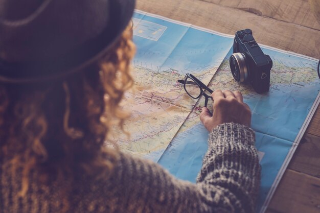 Photo curly lady viewed from rear planning next trip vacation wanderlust on a paper map and old camera on the table - planning holday and travel concept for hipster people at home - wanderlust and tenerife