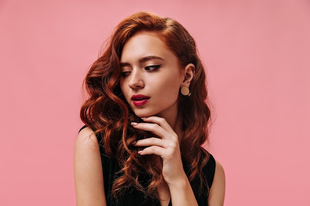 Curly lady with beautiful earrings poses in pink wall