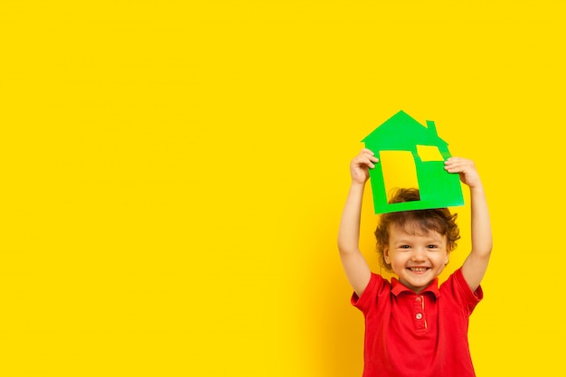 a curly laughing emotional kid holds a cardboard house of green color above his head