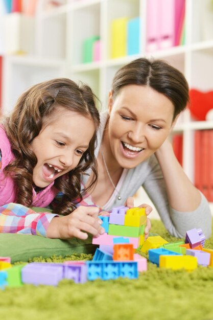 Curly little girl and her mother playing with colorful plastic blocks