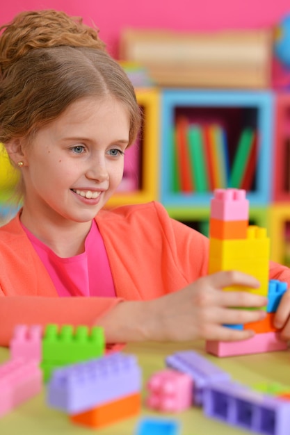 Curly little girl playing with colorful plastic blocks at home