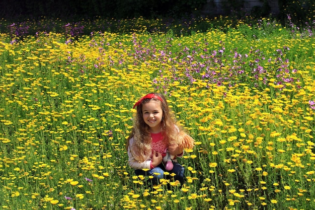 Foto bambina riccia con un fiocco rosso tra i capelli ragazza su un prato verde tra fiori gialli