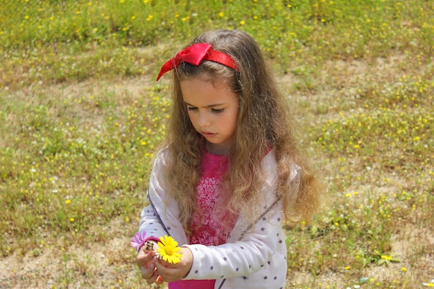 Foto bambina riccia con un fiocco rosso tra i capelli ragazza su un prato verde tra fiori gialli