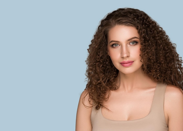 Foto ritratto di bellezza della donna dei capelli ricci lunghi del brunette, fronte di fascino femminile. colore sfondo blu