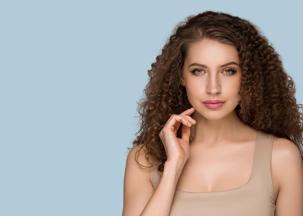 Curly long brunette hair young  woman touching face beauty  female portrait. Color backgound blue