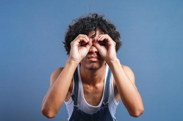 Curly man holding hands on eyes as if looking through binoculars or glasses with serious face