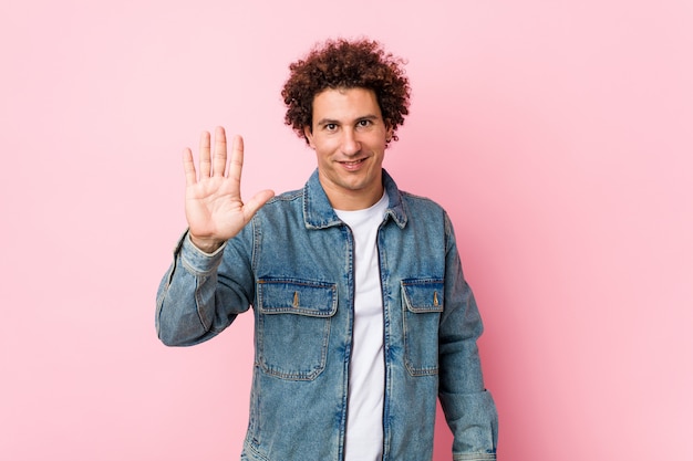 Curly mature man wearing a denim jacket against pink background smiling cheerful showing number five with fingers.