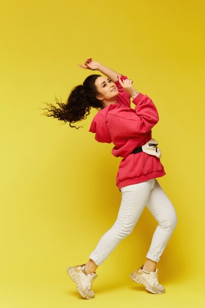 Curly model girl in pink oversized hoodie smiles on yellow background charming woman isolated at the yellow background