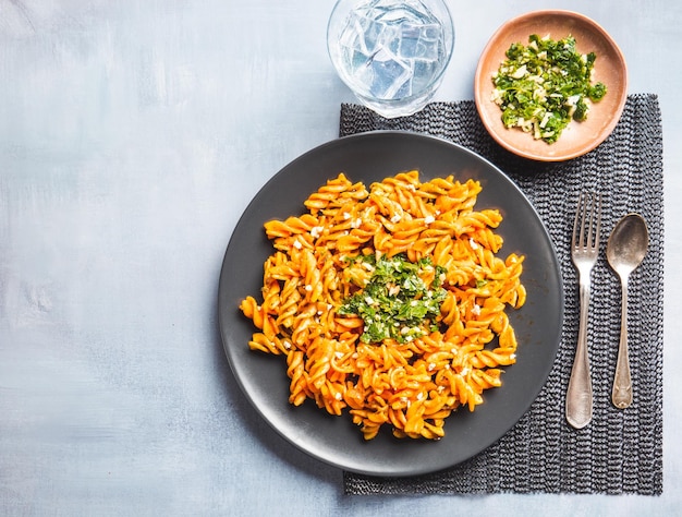 Curly pasta macaroni met tomaat en gremolata saus in een rond donker bord op tafel