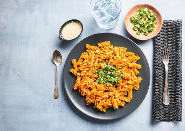 Curly pasta macaroni with tomato and gremolata sauce in a round dark plate on a table with cutlery a