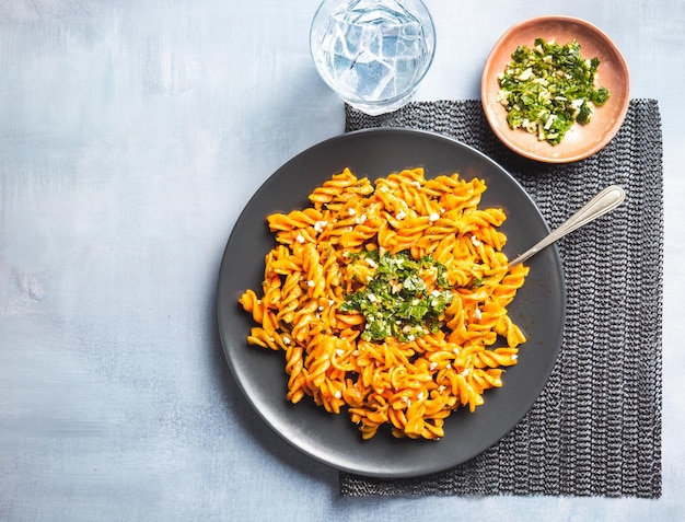 Curly pasta macaroni with tomato and gremolata sauce in a round dark plate on a table