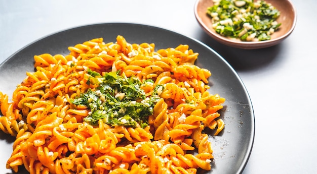 Photo curly pasta macaroni with tomato and gremolata sauce in a round dark plate on a table