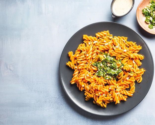 Curly pasta macaroni with tomato and gremolata sauce in a round dark plate on a table