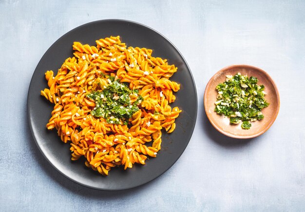 Photo curly pasta macaroni with tomato and gremolata sauce in a round dark plate on a table