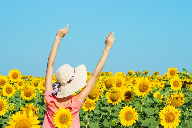 Curly pretty girl in hat having fun in field of yellow sunflowers