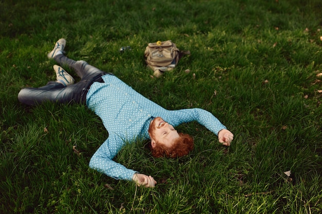 Curly reddish man in blue shirt lying on green grass