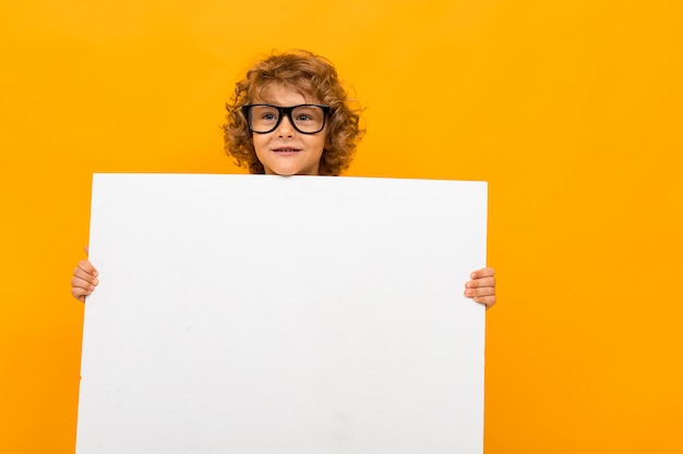 Curly schooljongen in glazen voor visie op een van een oranje muur heeft een grote lege vorm in zijn handen