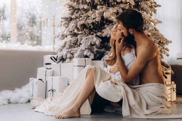 curly smiling woman hugging shirtless muscular boyfriend near christmas tree at home