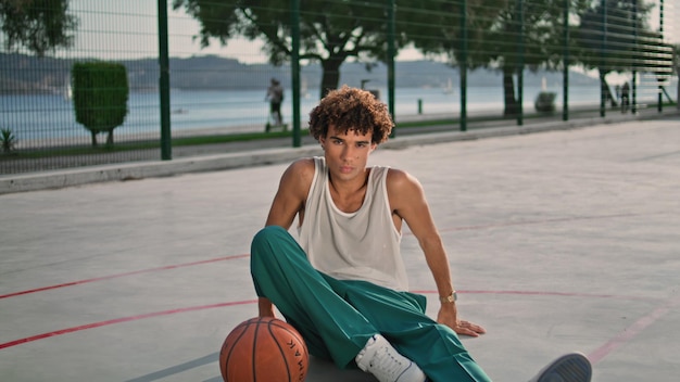 Фото Кудрявый спортсмен, сидящий на стадионе, увеличивает расслабляющий портрет баскетболиста