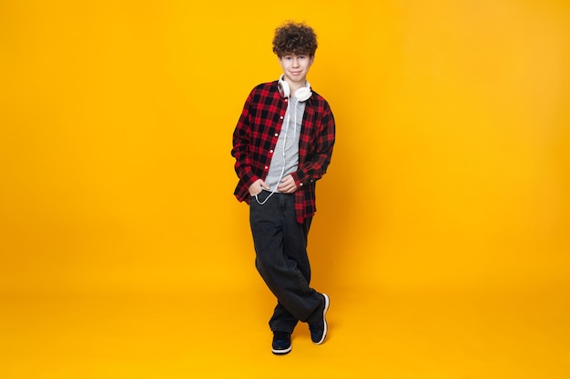 Curly teenager boy in headphones on a yellow background