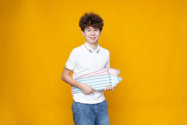 Curly teenager boy with pencils on a yellow background