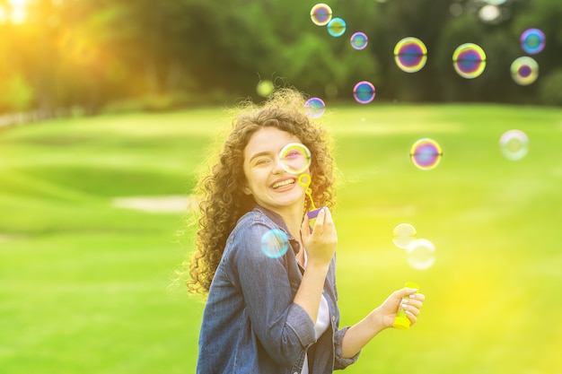 The curly woman blowing bubbles in the green park