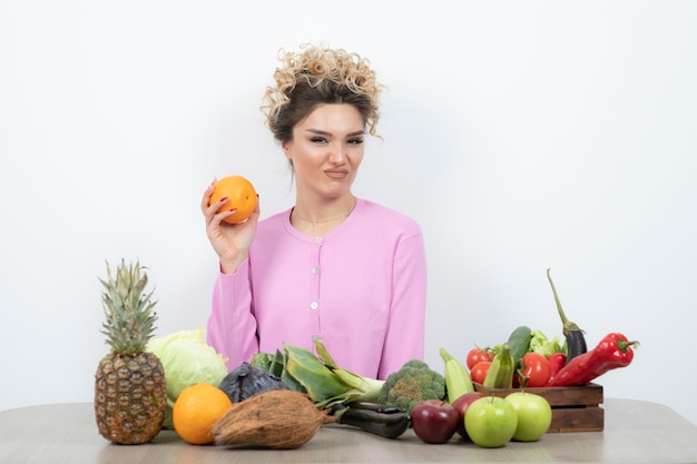 Curly woman sitting at table holding juicy orange.