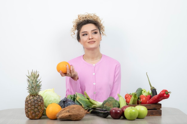 Curly woman sitting at table holding juicy orange.