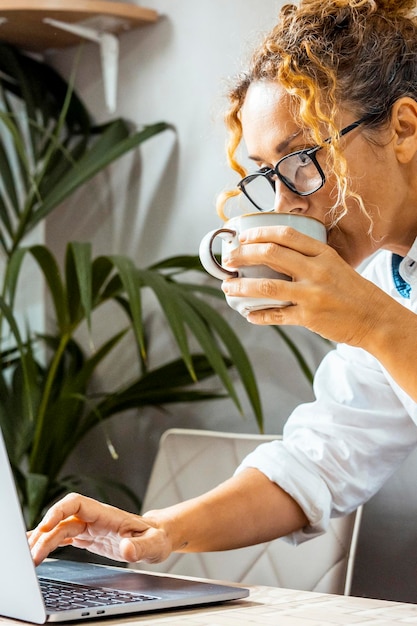 Curly woman with glasses using laptop communicating on Internet with client in home Cozy working office remote work elearning concept