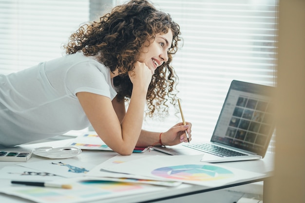 The curly woman working with a brush and a laptop