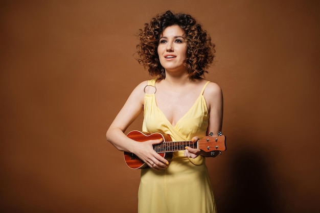 Curly woman in a yellow dress plays ukulele and sings a song