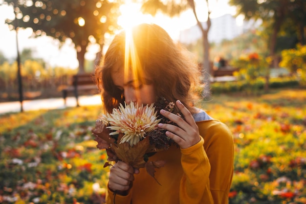 乾燥した葉と花の秋の花束と草の上の黄色いセーターの巻き毛の若い女の子