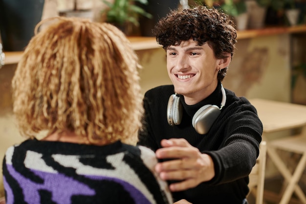 curly young man with wireless headphones touching shoulder of african american girl in vegan cafe