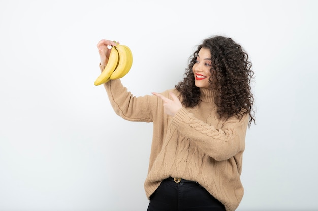 Photo curly young woman holding bananas over white.