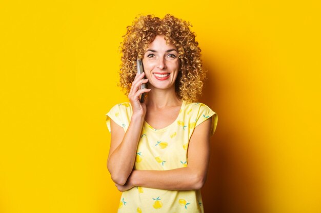 Curly young woman smiling talking on the phone on a yellow background Banner