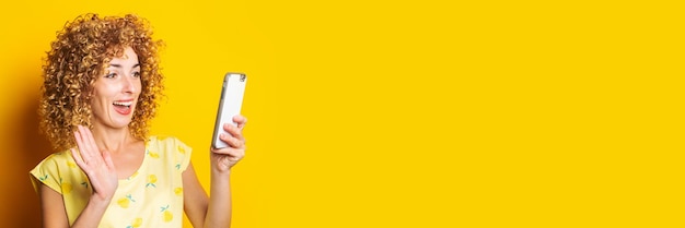 Curly young woman talking on video chat on the phone on a yellow background Banner