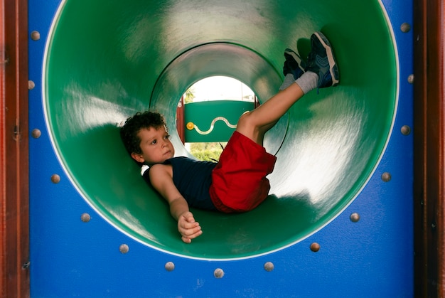 Curlyhaired boy lying inside a tube at a playground