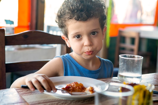 Photo curlyhaired caucasian boy eating in restaurant