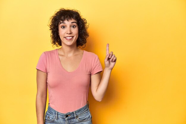 Foto donna caucasica dai capelli ricci con una maglietta rosa che mostra il numero uno con il dito