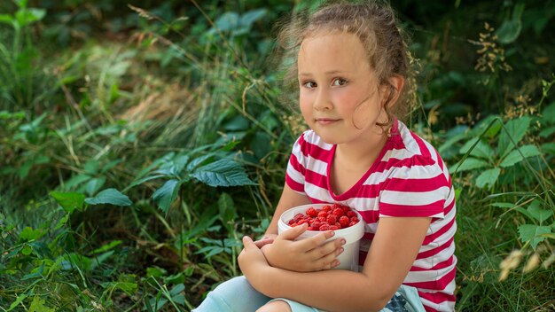 curlyhaired girl with berries sitting on the grass in the garden