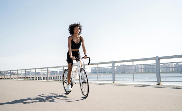 Кудрявая счастливая женщина ездит на велосипеде Велосипедист тысячелетия едет экологически чисто