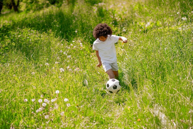 Curlyhaired jongen in witte sportkleding voetballen