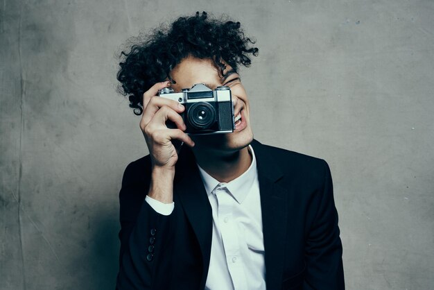 Curlyhaired man in a classic suit looks at the camera in his hand studio hobby