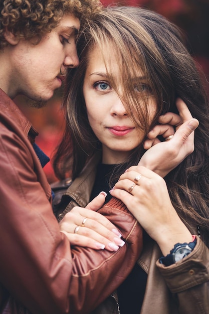 Curlyhaired mustachioed man and brownhaired woman hugging in autumn against background of red trees