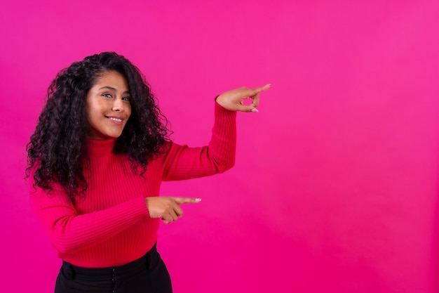 Curlyhaired vrouw die naar rechts wijst op een roze achtergrond studio shot copy paste