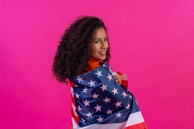 Curlyhaired woman embracing usa flag on a pink background studio shot